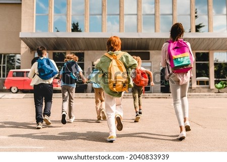 Little kids schoolchildren pupils students running hurrying to the school building for classes lessons from to the school bus. Welcome back to school. The new academic semester year start Royalty-Free Stock Photo #2040833939