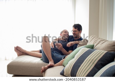 gay men couple in their day to day talking, playing on their cell phone, relaxed in their living room, in love and happy