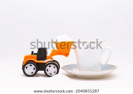 A miniature toy tractor plowing, lifting granulated sugar into a cup with a drink, tea or coffee on a white background. giving up sugar