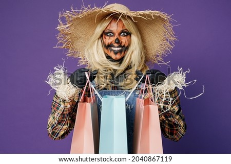 Young woman with Halloween makeup mask in straw hat scarecrow costume hold package bags with purchases after shopping isolated on plain dark purple background studio Celebration holiday party concept