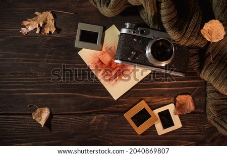 Autumn still life with an old camera, sweater, photos and fallen leaves on wooden background