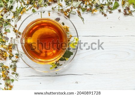 Cup of herbal tea with natural dried herbs on white wooden background.