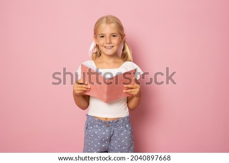 Beautiful girl with bond hair holds a notebook and smiles, picture isolated on pink background