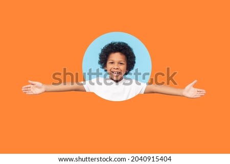 Let's hug. Portrait of friendly little boy with curls in white T-shirt smiling happily and holding hands wide open to embrace, welcome. indoor shot isolated in a round hole on orange background Royalty-Free Stock Photo #2040915404