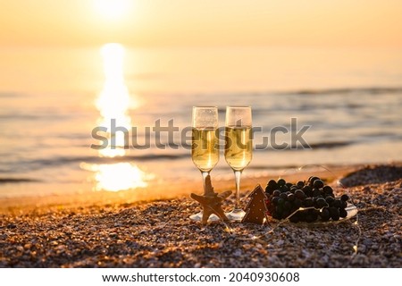 Celebrating Christmas on the seashore. Two glasses of champagne and cookies in the shape of a Christmas tree on a sunset background. Selective focus on the tree and glass.