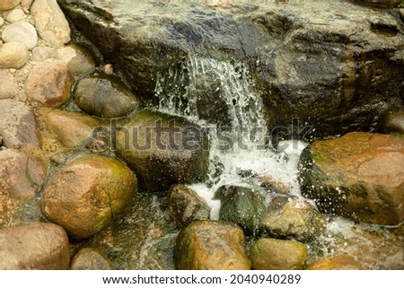 Waterfall among the stones. Artificial pond. Landscape design with stones and water. The flow of water through large cobblestones.