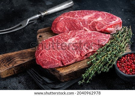 Fresh Raw Top Blade or flat iron beef meat steaks on a butcher cutting board. Black background. Top View Royalty-Free Stock Photo #2040962978