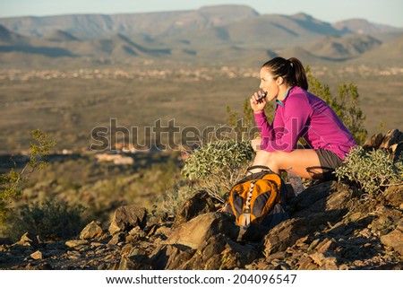 Young woman pauses at the top of a trail midway through her hike at Phoenix Sonoran Preserve in Phoenix, Arizona. She is having a snack. Royalty-Free Stock Photo #204096547