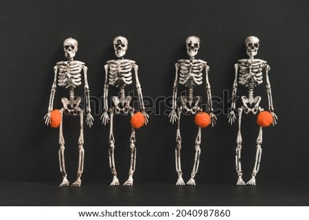 Four skeletons stand against a black background and hold small orange balls. Preparation for Halloween party. Modern Halloween or Day of the Dead concept. Copy space.