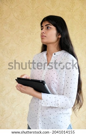 An Indian lady smiling with a tablet in her hands on a wall background