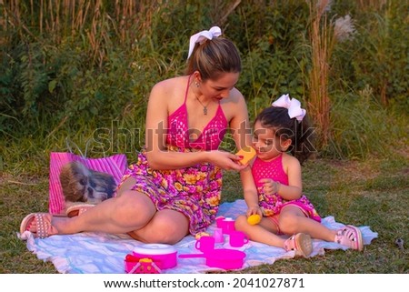 A cute happy small girl sitting on a picnic blanket with her mother and playing toys outdoor