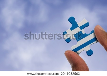 Hand holding piece of jigsaw puzzle with flag of Greece. Jigsaw puzzle of Greece flag on sky background.