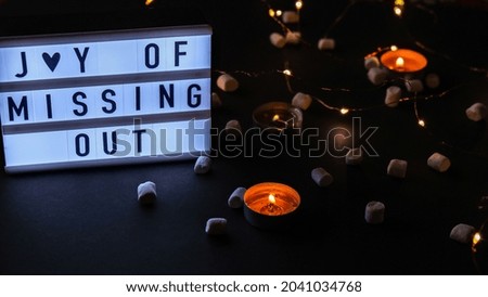 Lightbox with text JOMO Joy of Missing Out. The concept of relaxation from information and gadgets. Tea light candles. Digital detox