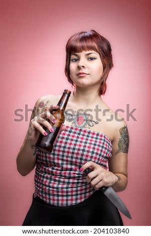 Young woman with tattoos holding beer and knife 