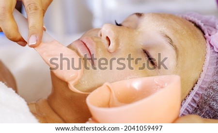 Cosmetologist applies  a scrub on female face. Woman in a spa salon on cosmetic procedures for facial care.