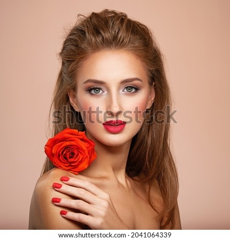 Beautiful young woman with a red flower in hand near face.  Portrait of white girl with red rose in hands. Beauty face concept. Art portrait of an attractive model. Girl with bright fashion makeup Royalty-Free Stock Photo #2041064339