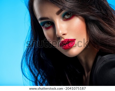 Portrait of beautiful young woman with bright blue makeup. Beautiful brunette with bright red lipstick on her lips. Pretty girl with long black hair. Closeup face of brunette woman. 
