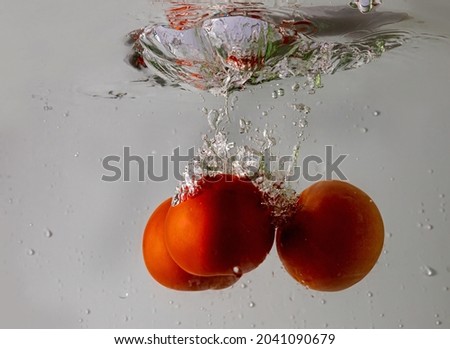 Ripe tomato falls deeply under water with a big splash.