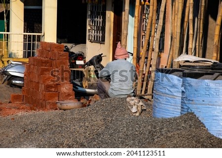 Stock photo of 50 to 60 old man is resting and sitting on pile of gray stones under bright sunlight during his job at construction site, at Kolhapur ,Maharashtra, India.