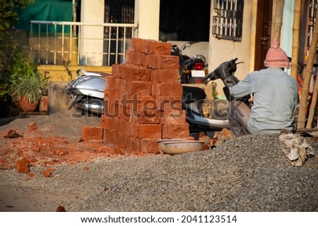 Stock photo of 50 to 60 old man is resting and sitting on pile of gray stones under bright sunlight during his job at construction site, at Kolhapur ,Maharashtra, India.