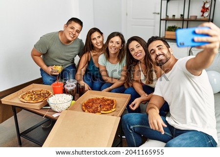 Group of young hispanic friends eating italian pizza make selfie. by the smartphone at home.
