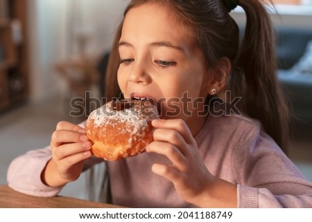 Happy little girl eating tasty donuts on Hannukah at home