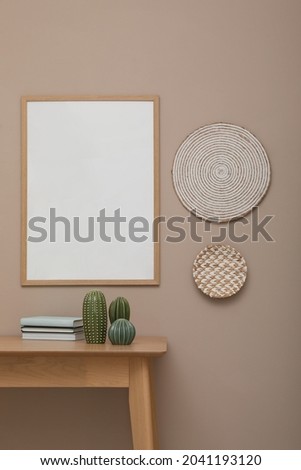 Empty frame hanging on beige wall over wooden table with decor. Mockup for design