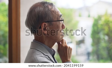 Elderly Asian man looking outside through a window.