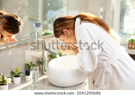 Morning routine. A beautiful woman in a bathrobe washes her face in the bathroom by the sink. Modern interior. Pregnancy. Reflection in the mirror. Clean skin Royalty-Free Stock Photo #2041200686
