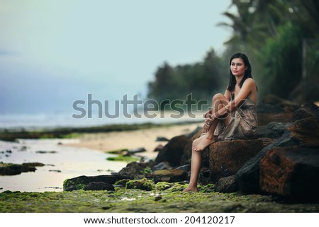 Woman sits on rocky summit above sea, looking at the camera