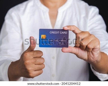 Hand of holding a mockup blue credit card and thumbs up while standing with a black background in the studio. Close-up photo. Money and business concept.
