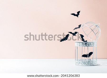 Creative minimal concept with white bird cage and bats silhouettes on pastel background. Halloween scary concept with copy space. Modern aesthetic.