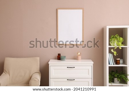 Empty frame hanging on pale rose wall over chest of drawers in living room. Mockup for design