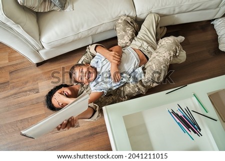 Little boy having fun at the floor with his multiracial soldier mother