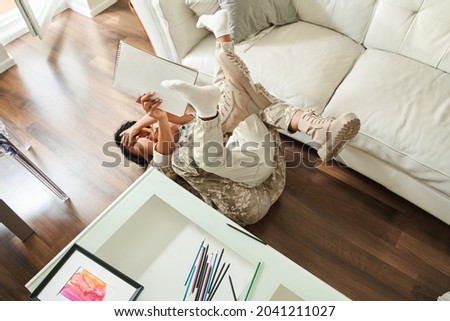 Little boy having fun at the floor with his multiracial soldier mother while meet her