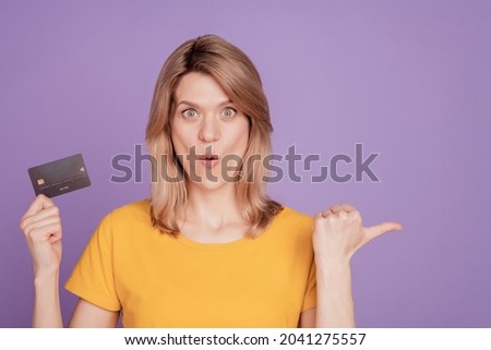 Photo of young attractive woman amazed shocked credit card point thumb empty space isolated on violet color background