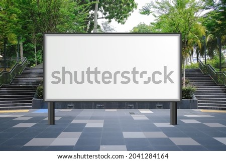 Large blank advertising poster billboard banner mockup in front of stairs; lush plants and tress in background; digital light box display screen for OOH media. Speckled textured concrete cement ground Royalty-Free Stock Photo #2041284164