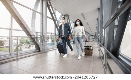 Young Arab Couple Wearing Medical Masks Walking With Luggage In Airport Hallway, Middle Eastern Spouses Holding Hands And Going To Boarding Gate, Travelling Together During Coronavirus Pandemic Royalty-Free Stock Photo #2041285727