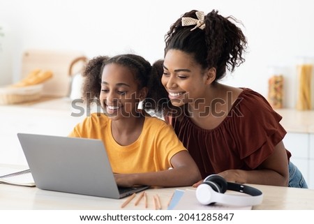 Cute black mother and kid using laptop together, sitting at kitchen table, hugging and looking at computer screen, spending time together, watching cartoon, copy space, closeup photo