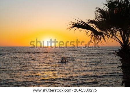 Two girls sit on sup board in the quiet mediterranean sea at sunset in the city of paphos in cyprus. Silhouettes of 2 girl paddling on paddle board at sunset. Water sport near the beach on sunset.
