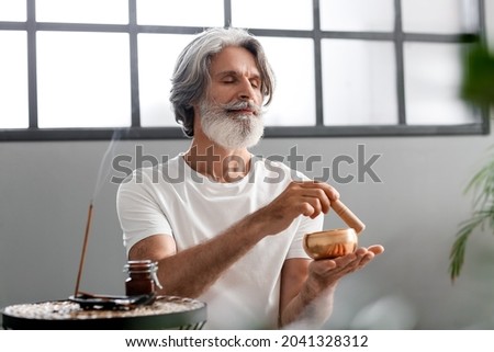 Mature man with Tibetan singing bowl at home Royalty-Free Stock Photo #2041328312