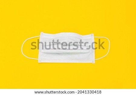 White medical disposable mask isolated on yellow background. Close-up. Banner. Copy space. Mockup design. Flat lay. Layout. Personal respiratory system protective equipment. Used material. Filtration.