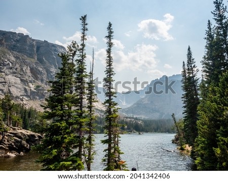 Pine trees in foreground of a nature scene with clouds reflecting on a lake in the Rockies.