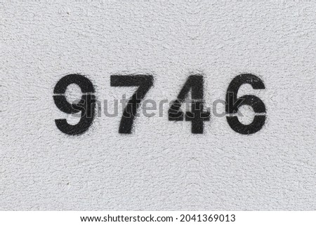 Black Number 9746 on the white wall. Spray paint. Number nine thousand seven hundred forty six.