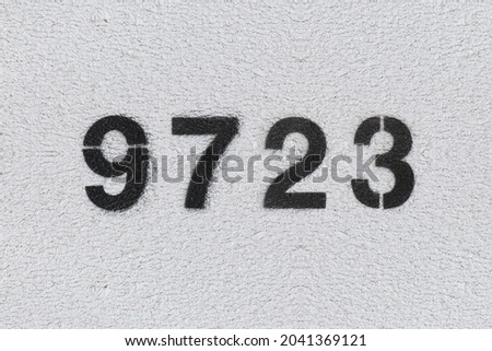 Black Number 9723 on the white wall. Spray paint. Number nine thousand seven hundred twenty three.