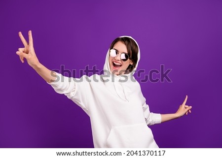 Photo of pretty shiny young lady wear white jumper dark eyewear smiling dancing showing -sign isolated purple color background