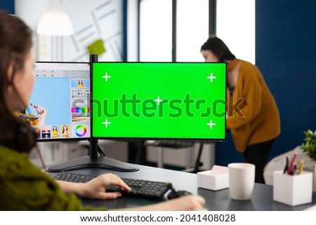 Photo artist retoucher editing assets in digital retouching program working in production agency studio. Photographer woman looking in computer with green screen, chroma key mockup isolated display.