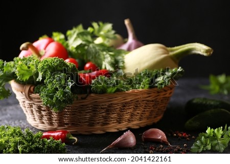 Harvest. Fresh herbs and vegetables. Curly kale cabbage, parsley, celery, red pepper, cucumbers, zucchini, garlic in a basket on a black table. Background image, copy space