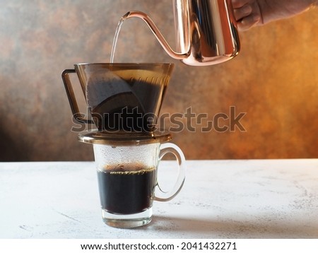 Brewed drip coffee making theme hand of barista pouring hot water onto ground coffee beans contained in paper filter, then allowing to brew. Aromatic hot drink preparation and brewing process.
