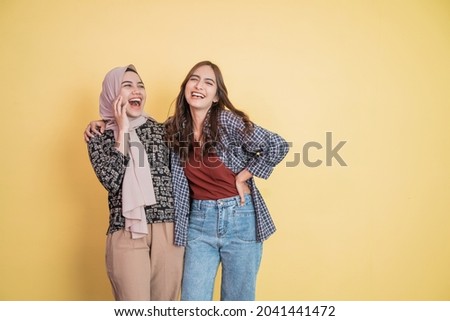 two beautiful muslim women laughing and joking while embracing with hands on shoulders with copyspace